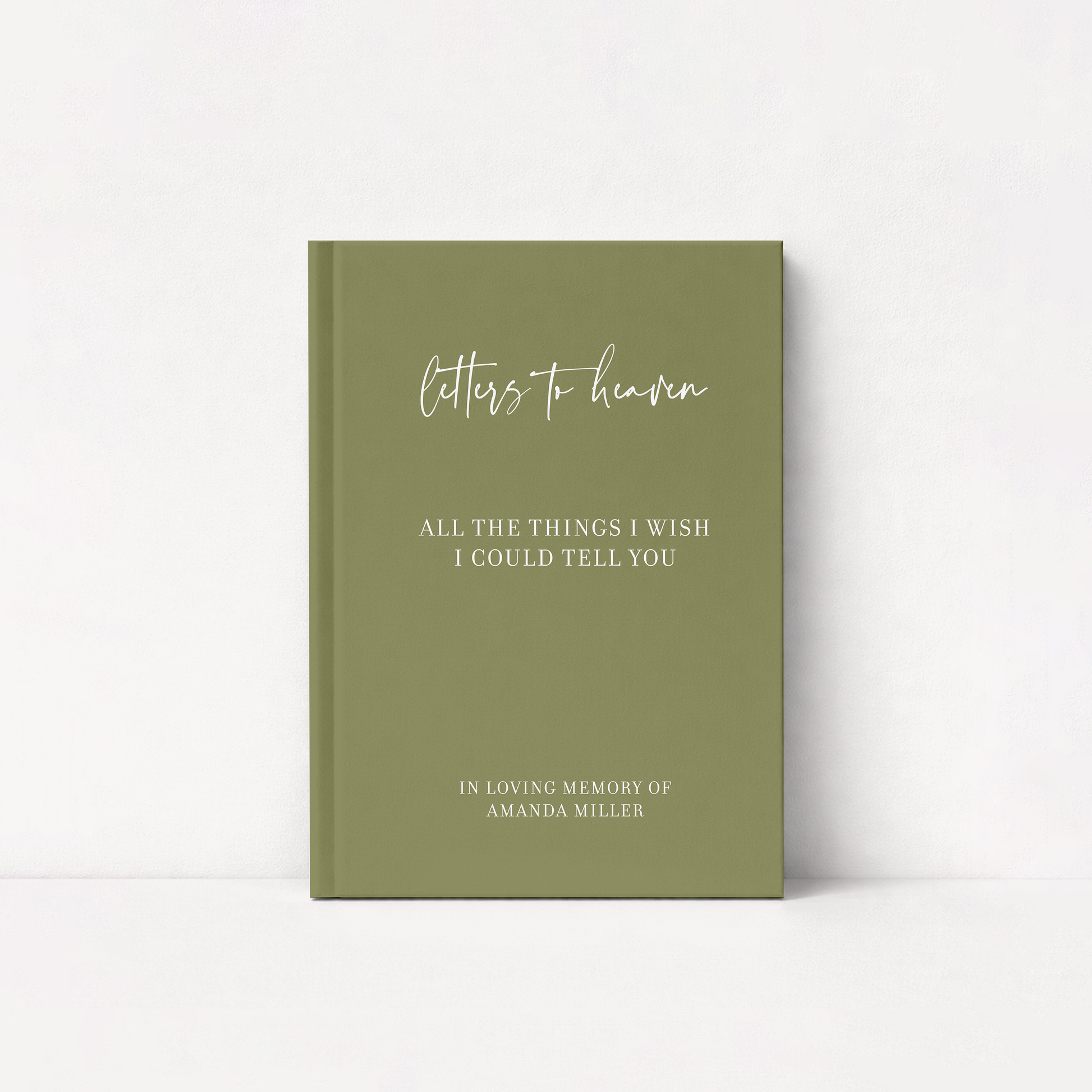 An olive green hardcover journal standing upright against a white background. The front cover features white text reading 'letters to heaven' in a cursive font, followed by 'ALL THE THINGS I WISH I COULD TELLYOU' and 'IN LOVING MEMORY OF AMANDA MILLER' in a serif font.
