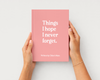 A pink hardcover book held by two hands against a light gray background. The book cover features the white text 'Things I hope I never forget.