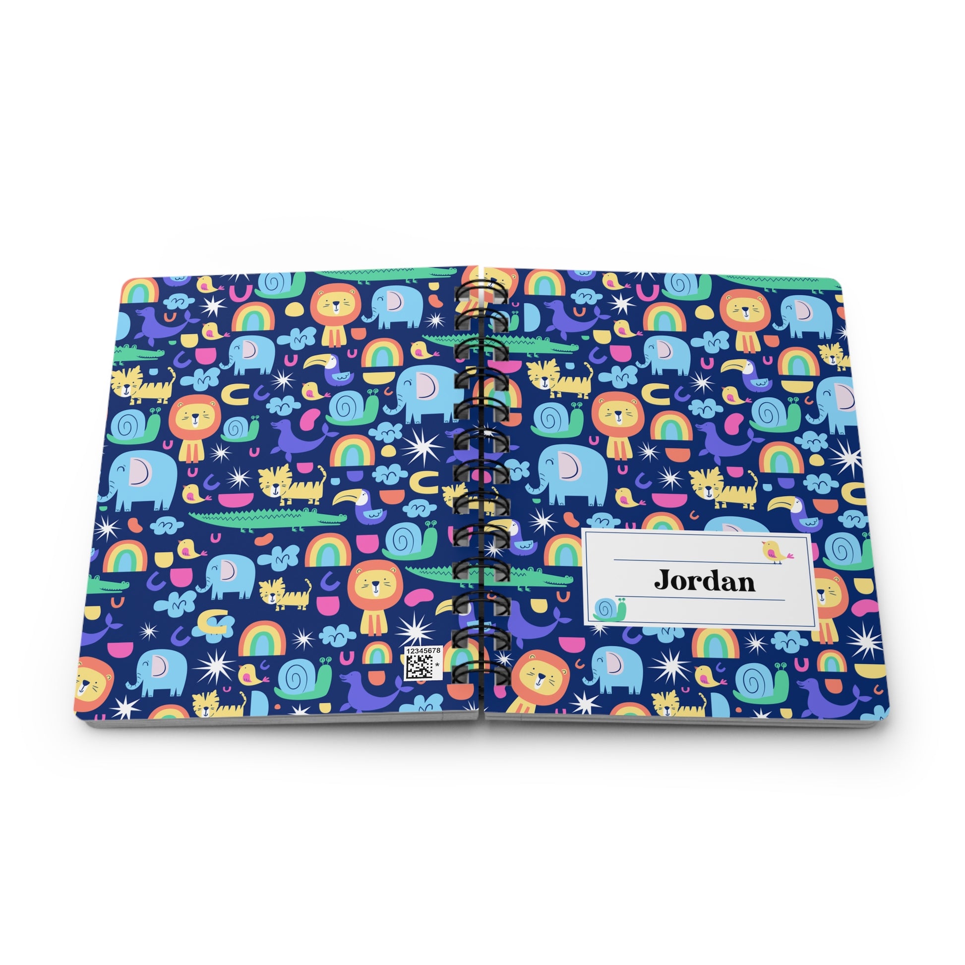 A personalized spiral-bound notebook with a colorful cartoon pattern of animals, rainbows, and stars on a dark blue background. The cover has a white label with the name 'Jordan' printed on it.