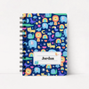 A spiral-bound notebook with a dark blue cover featuring a colorful cartoon safari pattern of lions, elephants, rainbows, and snakes. A white label on the front reads 'Jordan'.