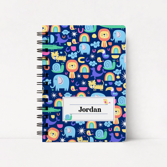A spiral-bound notebook with a dark blue cover featuring a colorful cartoon safari pattern of lions, elephants, rainbows, and snakes. A white label on the front reads 'Jordan'.