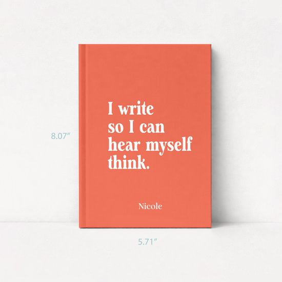 A coral orange hardcover book with white text reading 'I write so I can hear myself think.' and the name 'Nicole' at the bottom, shown standing against a white wall.
