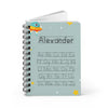 A personalized spiral-bound notebook with a light blue cover featuring the name 'Alexander' and the alphabet in dotted lines, decorated with a cartoon rocket and stars.