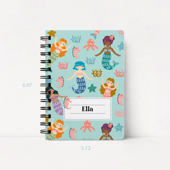A spiral-bound notebook with a light blue cover decorated with cartoon mermaids, fish, and coral, featuring a white label that says 'Ella'. The notebook is shown on a white background with dimension markings of 6.