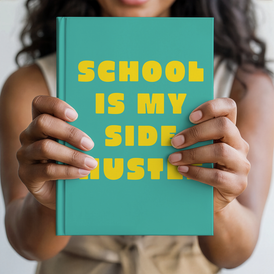 A person holding a teal notebook with bold yellow text that reads 'SCHOOL IS MY SIDE HUSTER' against a soft, blurred background.
