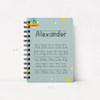 A spiral-bound notebook with a light blue cover featuring a cartoon alien and stars, personalized with the name 'Alexander' and alphabet tracing text. Height and width dimension markers are shown on the left and bottom.