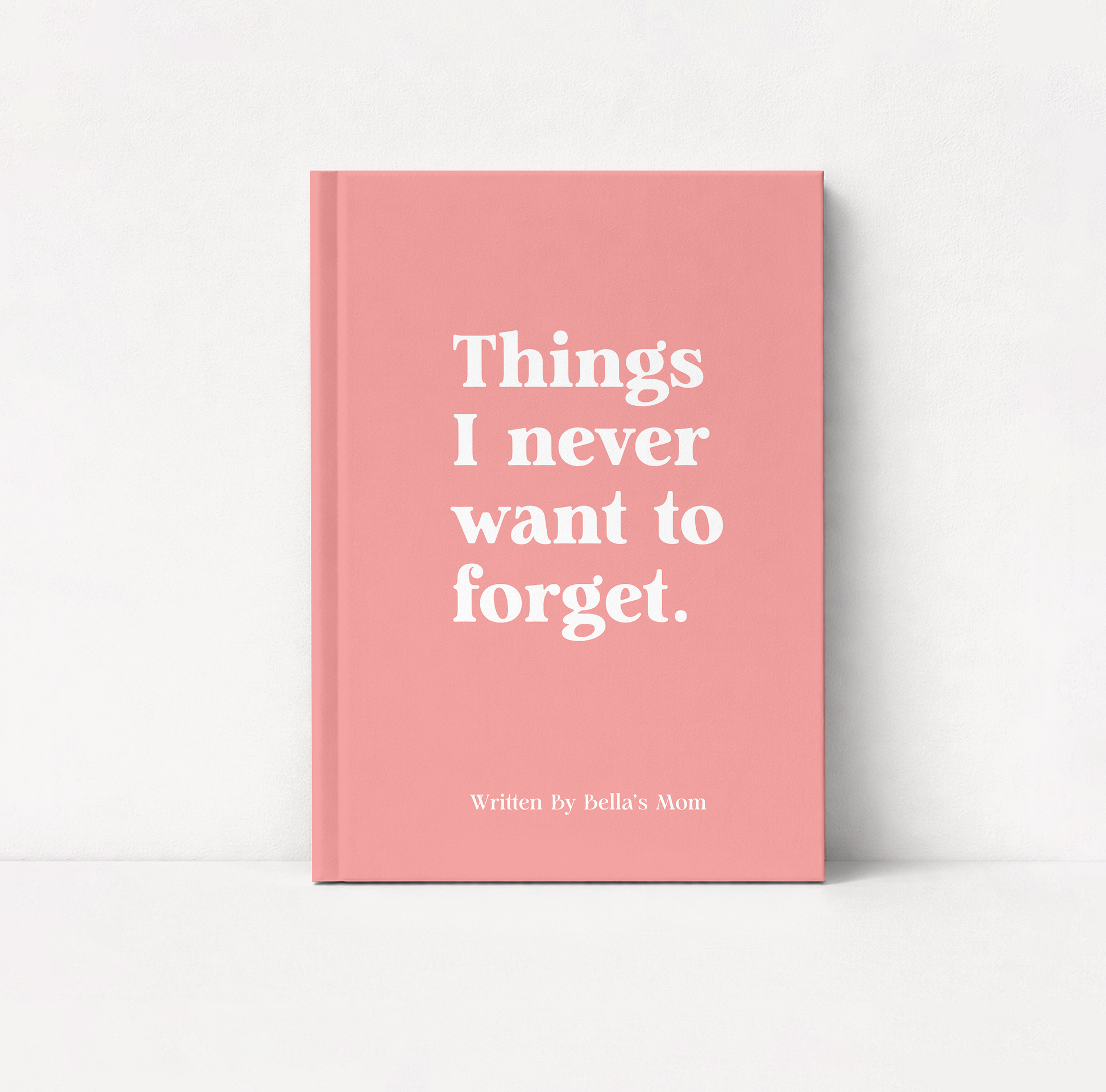 A pink hardcover notebook or journal standing upright on a white surface against a white wall. The front cover has large white serif text reading 'Things I never want to forget.