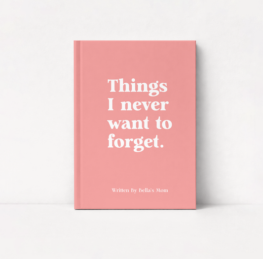 A pink hardcover notebook or journal standing upright on a white surface against a white wall. The front cover has large white serif text reading 'Things I never want to forget.