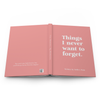 An open hardcover book with a dusty pink cover and white text reading 'Things I never want to forget. Written By Bella's Mom' on a white background.