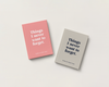 Two hardcover books with quote covers arranged on a light warm gray background. One book has a pink cover with white text, and the other has a light gray cover with dark navy text.