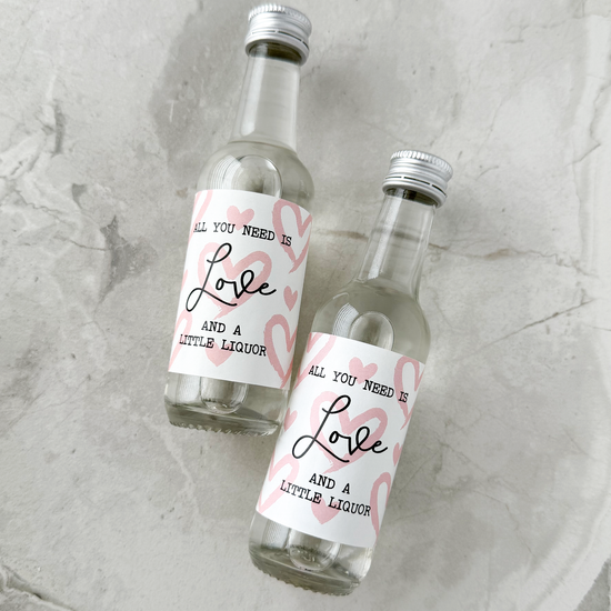 Two small liquor bottles with valentine day abels on a textured surface