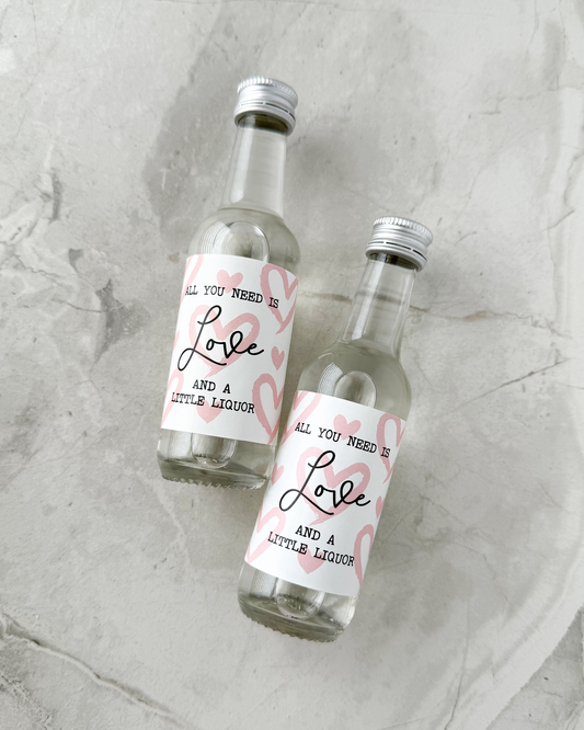 Two small liquor bottles with valentine day abels on a textured surface