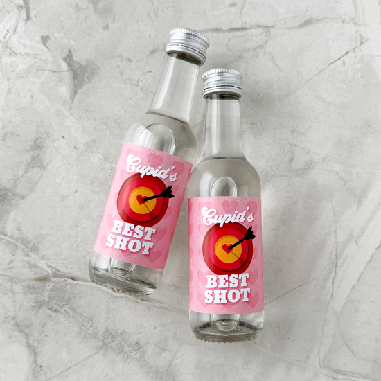 Two small liquor bottles labeled 'Cupid's Best Shot' on a gray marble surface. Valentine Party Favors