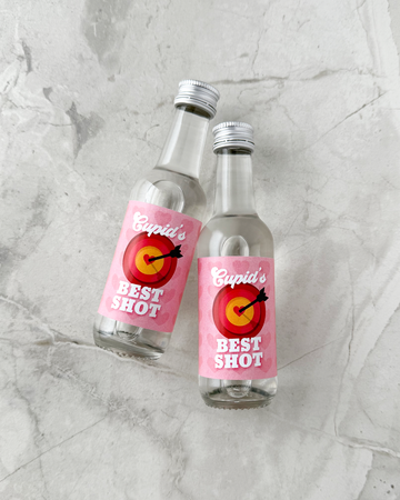 Two small liquor bottles labeled 'Cupid's Best Shot' on a gray marble surface. Valentine Party Favors