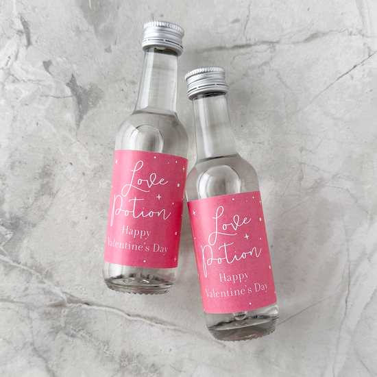 Two small glass bottles with pink 'Love Potion' labels on a gray marble surface.